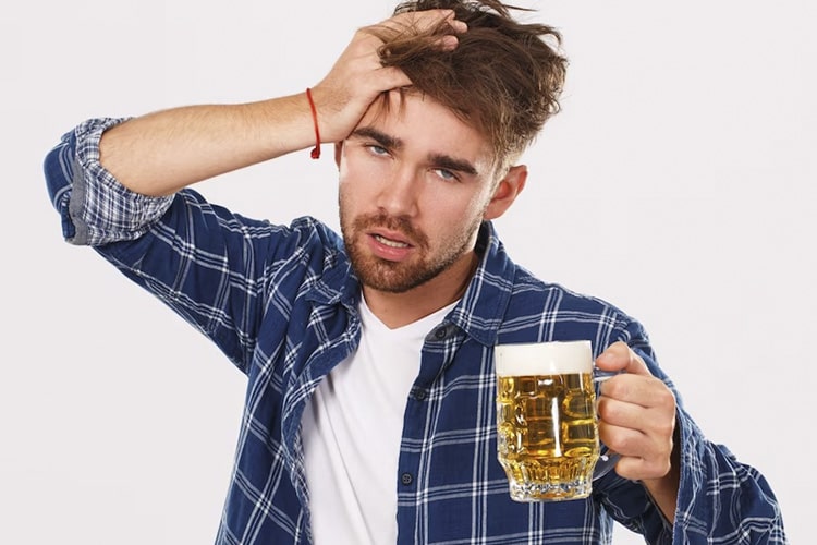 Мужчина держится за голову с кружкой пива